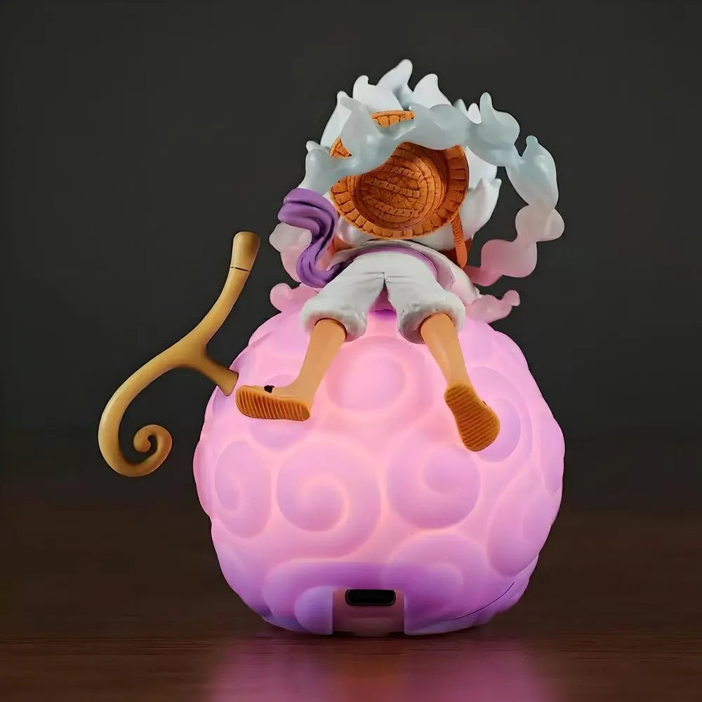 A back view of a Luffy Gear 5 Nika figure lying on a large, glowing pink One Piece devil fruit night light, showing his Straw Hat and white smoke curls against a dark background