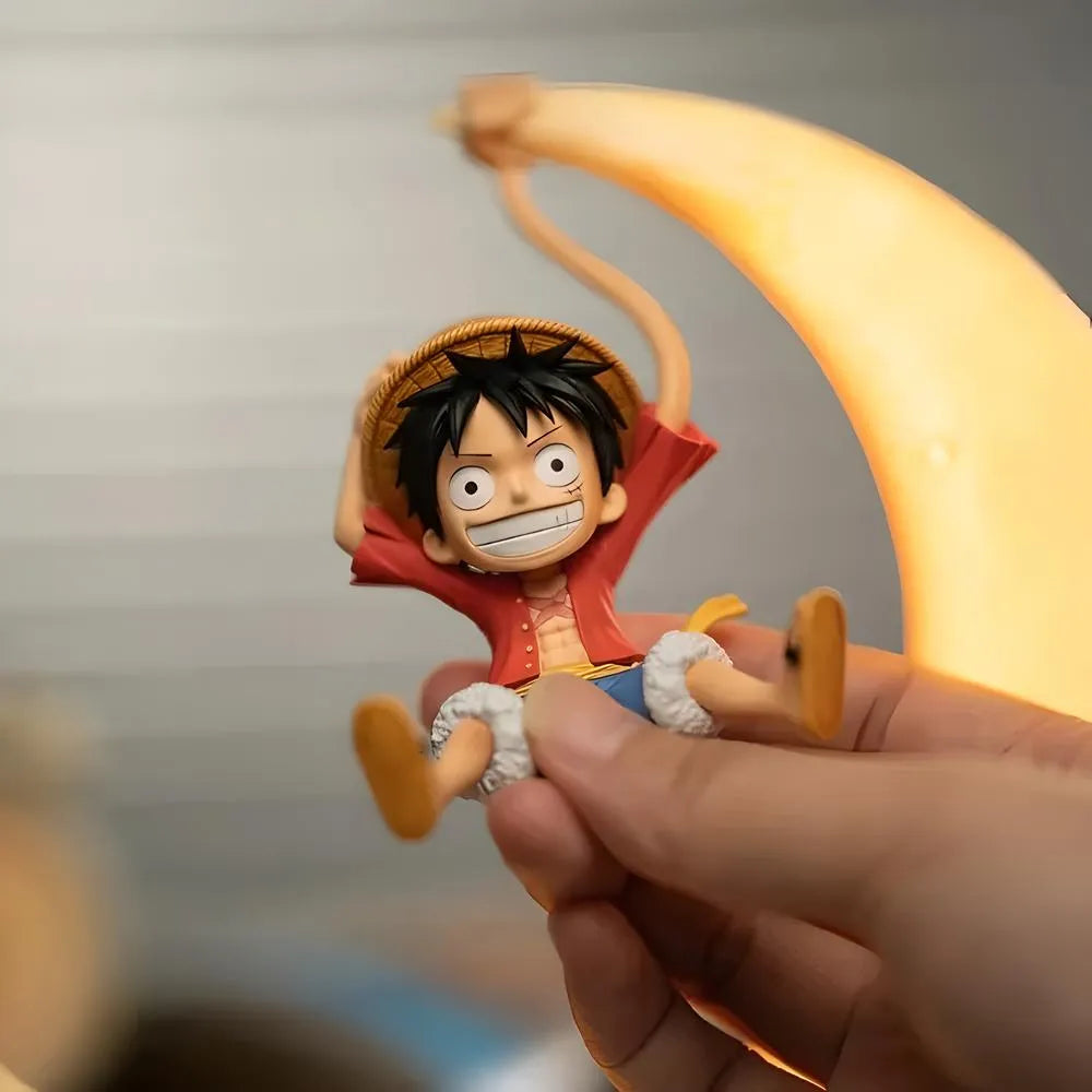 A hand holds a Luffy figure next to a glowing crescent moon lamp