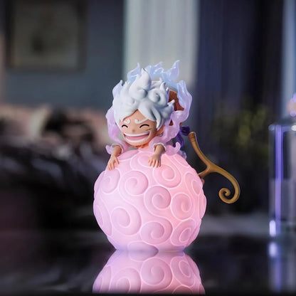 A front-facing view of a Luffy Gear 5 Nika figure, with his Straw Hat on his back, sitting happily on a large, glowing pink One Piece devil fruit night light in a room setting